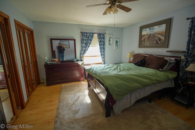 bedroom featuring ceiling fan, two closets, light hardwood / wood-style flooring, and a textured ceiling