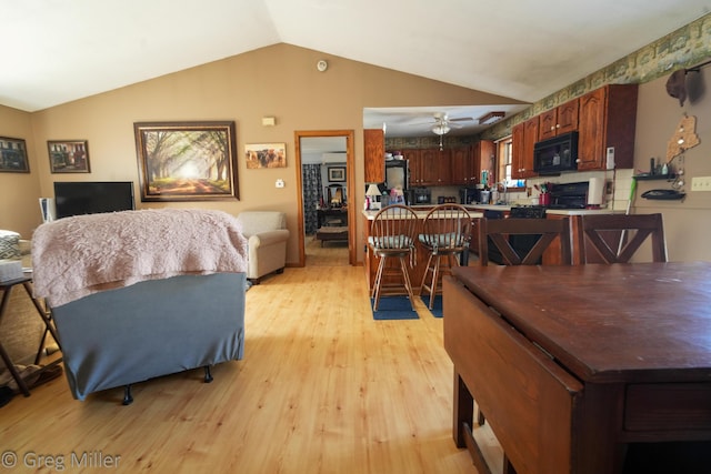 dining room with ceiling fan, vaulted ceiling, and light wood-type flooring