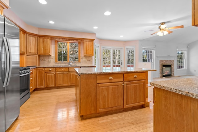 kitchen featuring brown cabinetry, a kitchen island, open floor plan, stainless steel appliances, and light wood-style floors