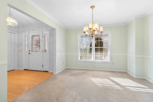 unfurnished dining area with crown molding, carpet floors, a decorative wall, and a notable chandelier