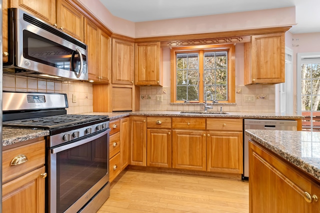 kitchen featuring appliances with stainless steel finishes, brown cabinetry, a sink, and light stone countertops