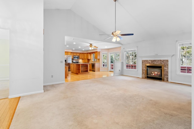 unfurnished living room featuring high vaulted ceiling, light carpet, baseboards, and a premium fireplace