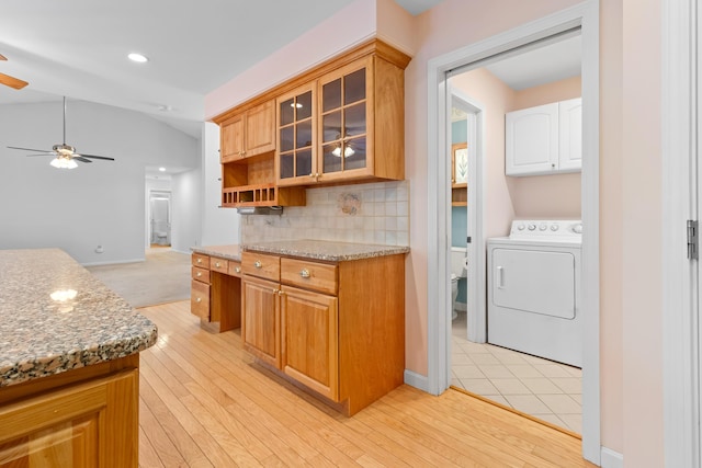 kitchen with glass insert cabinets, washer / clothes dryer, brown cabinets, light stone counters, and backsplash