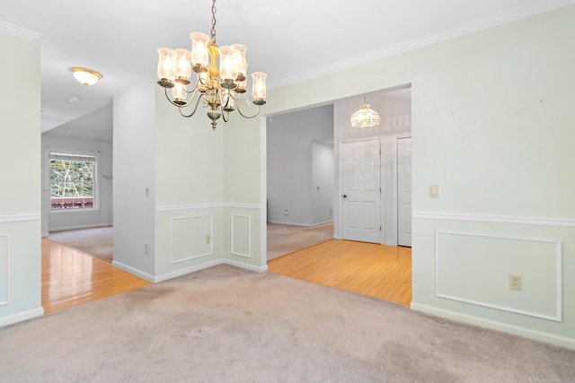 carpeted empty room featuring a wainscoted wall, a chandelier, a decorative wall, and crown molding