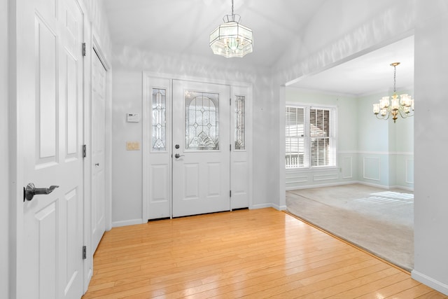 foyer with wainscoting, a decorative wall, light wood-type flooring, and an inviting chandelier