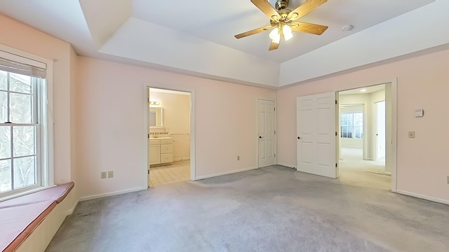 unfurnished bedroom featuring light carpet, multiple windows, and a raised ceiling