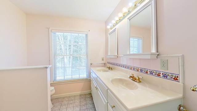 bathroom with baseboards, a sink, toilet, and double vanity