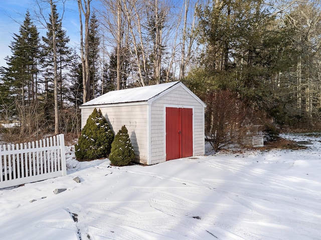 snow covered structure featuring fence, an outdoor structure, and a shed