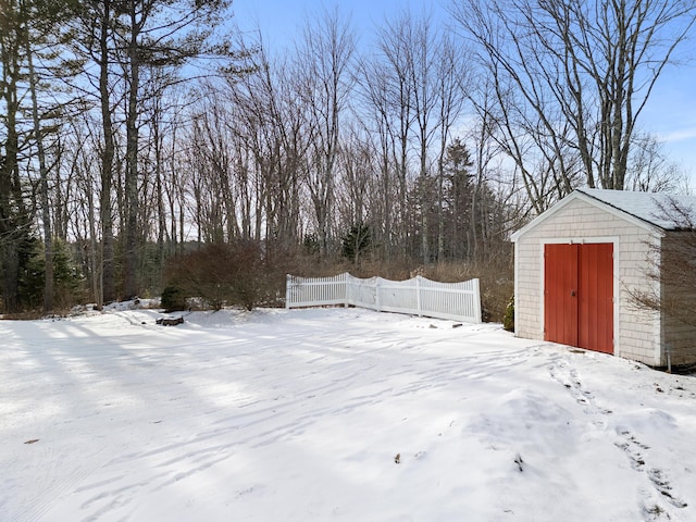 yard layered in snow featuring an outbuilding, fence, and a shed