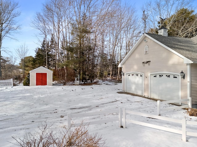 yard layered in snow featuring an outbuilding, a storage unit, and a garage