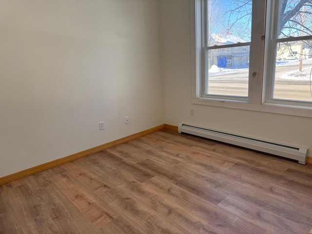 unfurnished room featuring a baseboard heating unit and light hardwood / wood-style floors