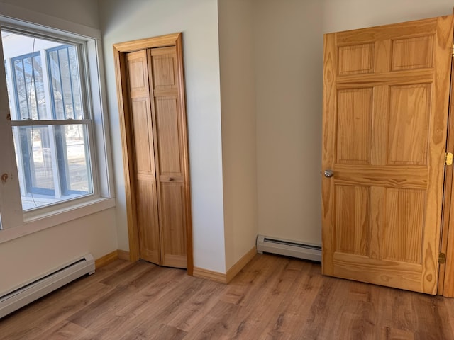 unfurnished bedroom featuring multiple windows, a baseboard heating unit, and light hardwood / wood-style floors