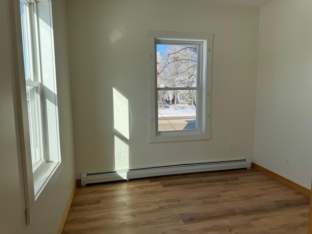 unfurnished room with a baseboard heating unit, dark hardwood / wood-style floors, and a healthy amount of sunlight