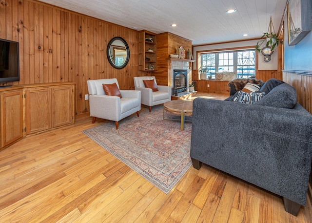 living room featuring a tile fireplace, ornamental molding, light hardwood / wood-style floors, and wood walls