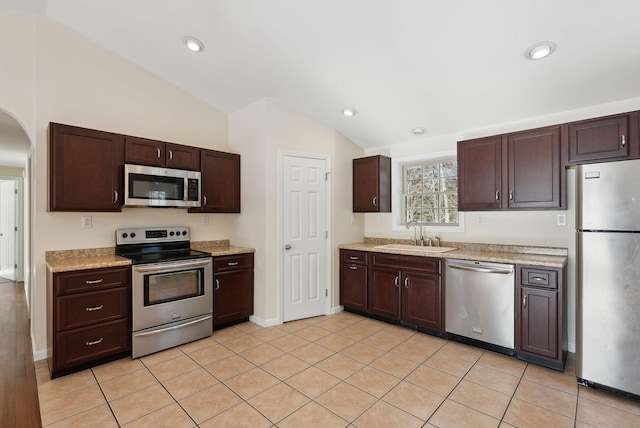 kitchen featuring vaulted ceiling, appliances with stainless steel finishes, sink, light tile patterned floors, and dark brown cabinetry