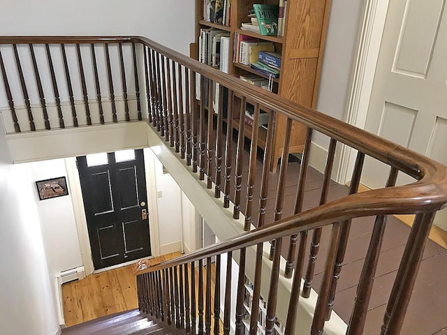 staircase with a baseboard heating unit and wood-type flooring