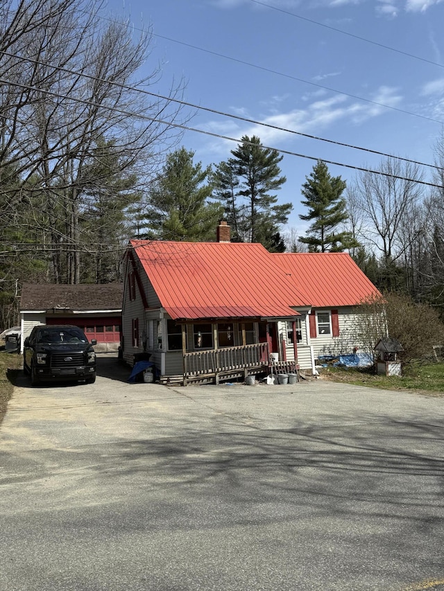 view of front of property with a porch, driveway, a chimney, and metal roof
