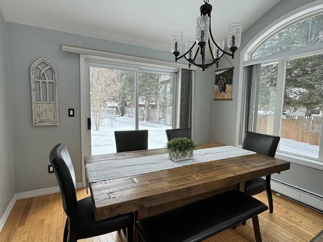 dining space with a baseboard heating unit, a healthy amount of sunlight, a notable chandelier, and light wood-type flooring