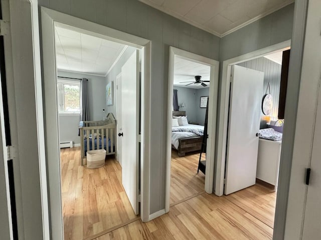 corridor with a baseboard radiator, ornamental molding, and light wood-type flooring