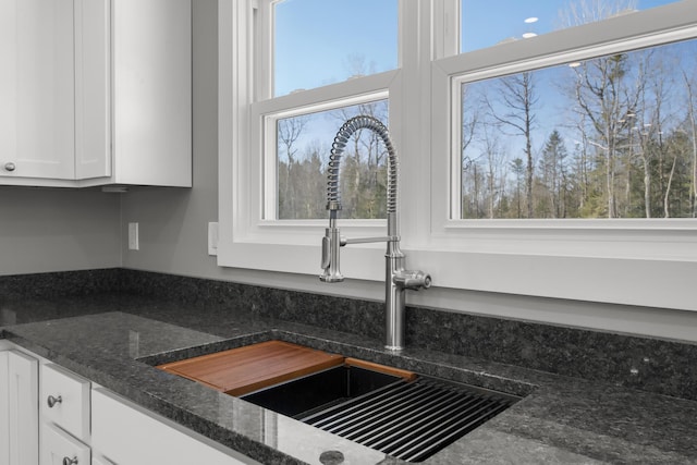 details with dark stone counters, sink, and white cabinets