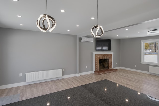 unfurnished living room with a brick fireplace, radiator heating unit, an AC wall unit, and light wood-type flooring