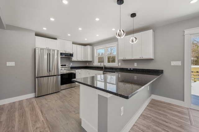 kitchen with appliances with stainless steel finishes, decorative light fixtures, white cabinets, kitchen peninsula, and light wood-type flooring