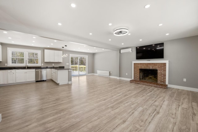 unfurnished living room with a brick fireplace, sink, a wall mounted AC, and light hardwood / wood-style flooring