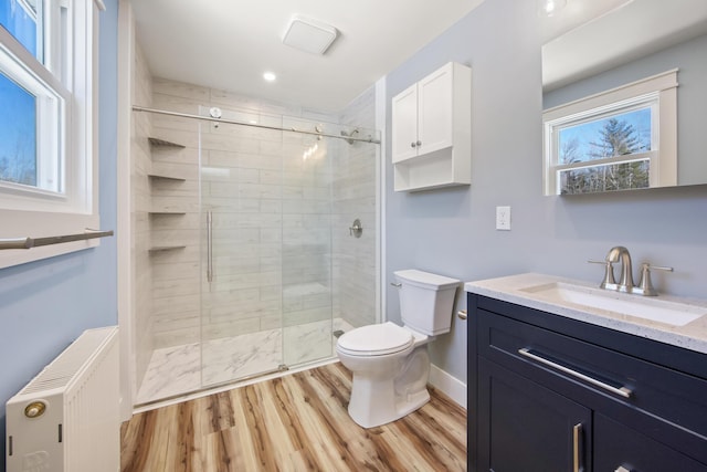 bathroom featuring radiator, a shower with shower door, hardwood / wood-style flooring, vanity, and toilet