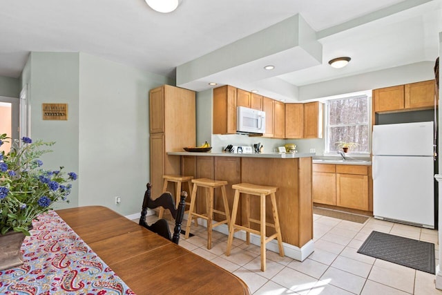 kitchen with white appliances, sink, light tile patterned flooring, kitchen peninsula, and a breakfast bar area