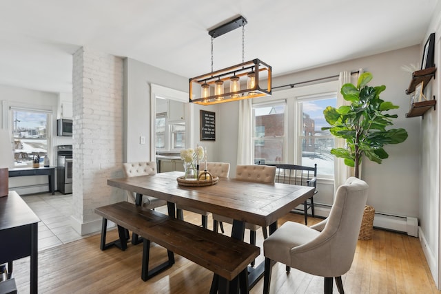 dining space featuring decorative columns, a brick fireplace, a baseboard heating unit, and light wood-type flooring