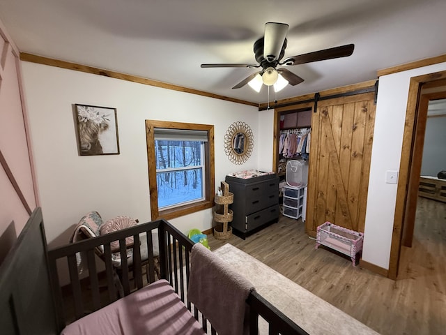 bedroom with hardwood / wood-style flooring, ornamental molding, ceiling fan, a barn door, and a closet