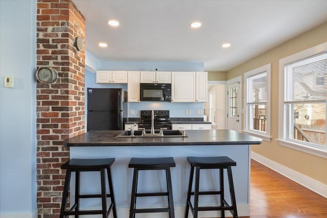 kitchen with hardwood / wood-style flooring, white cabinets, a breakfast bar, and black appliances