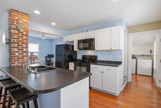 kitchen with washing machine and clothes dryer, sink, a breakfast bar area, white cabinetry, and black appliances