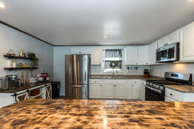 kitchen with wooden counters, a sink, appliances with stainless steel finishes, white cabinetry, and crown molding