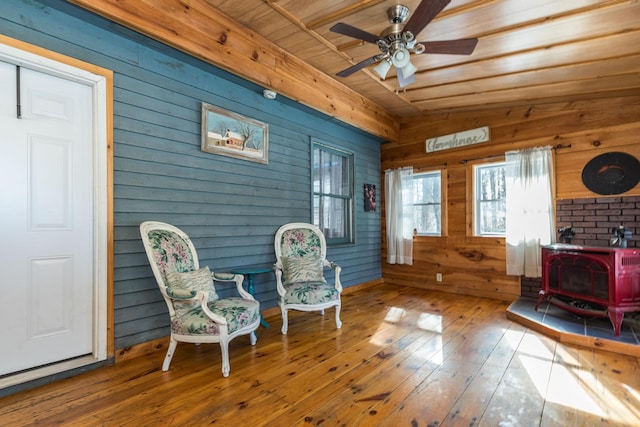 living area with hardwood / wood-style floors, a ceiling fan, lofted ceiling, a wood stove, and wood walls