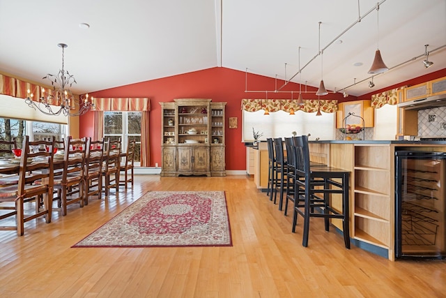 dining room featuring light wood-style floors, beverage cooler, vaulted ceiling, and a dry bar