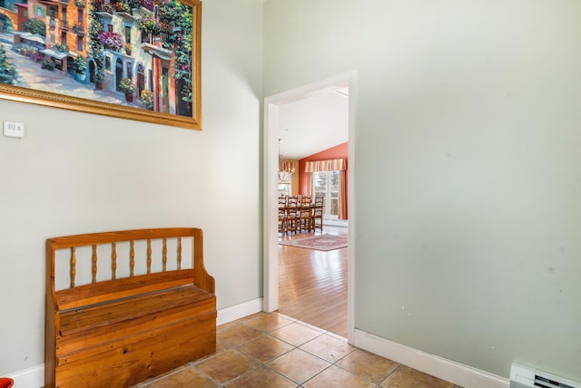 hallway with vaulted ceiling, baseboard heating, tile patterned flooring, and baseboards