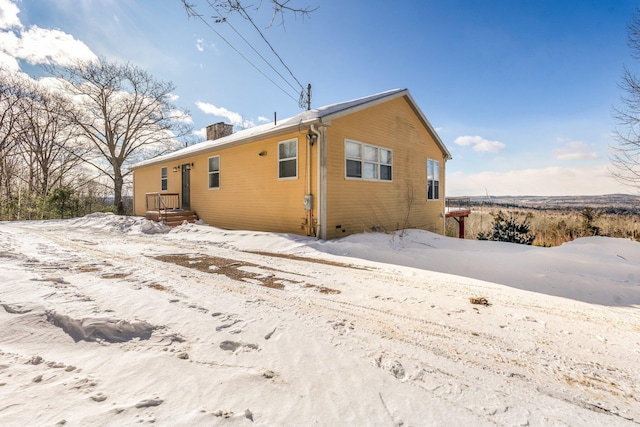 snow covered rear of property featuring crawl space and a chimney