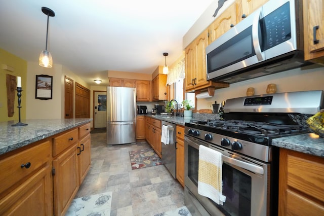 kitchen with appliances with stainless steel finishes, sink, hanging light fixtures, and dark stone counters