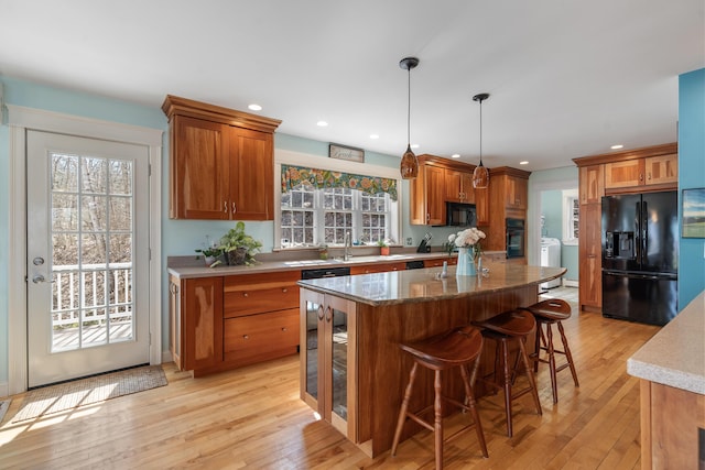 kitchen with decorative light fixtures, a kitchen bar, a center island, black appliances, and light wood-type flooring