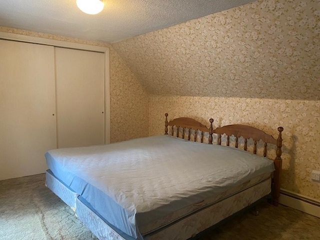 bedroom with vaulted ceiling, a textured ceiling, dark carpet, a closet, and a baseboard heating unit