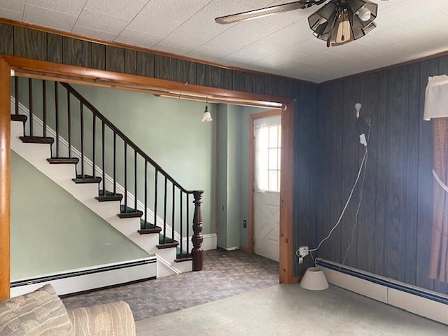 entrance foyer featuring baseboard heating, ceiling fan, wooden walls, and carpet