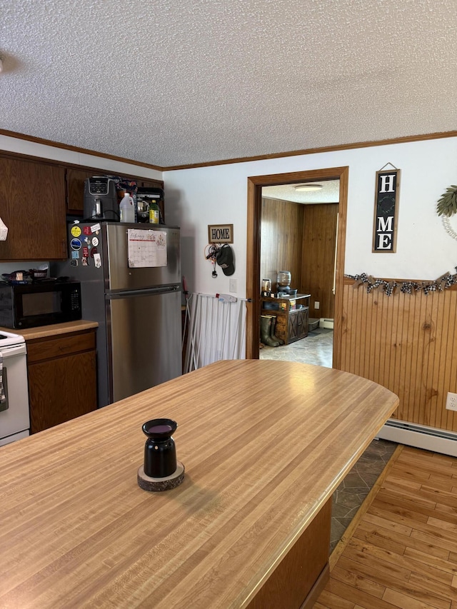 dining room with crown molding, a baseboard heating unit, wooden walls, a textured ceiling, and light wood-type flooring