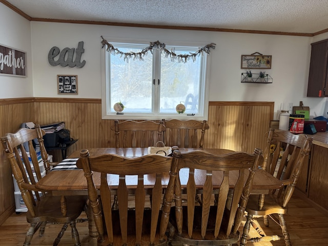 dining space featuring wood-type flooring, ornamental molding, wooden walls, and a textured ceiling