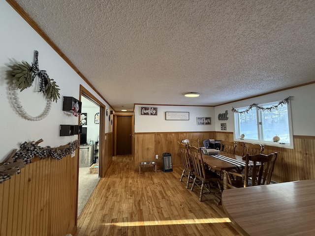 dining space with crown molding, a textured ceiling, light wood-type flooring, and wood walls