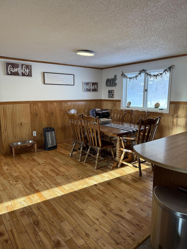 dining room with crown molding, wooden walls, light hardwood / wood-style floors, and a textured ceiling