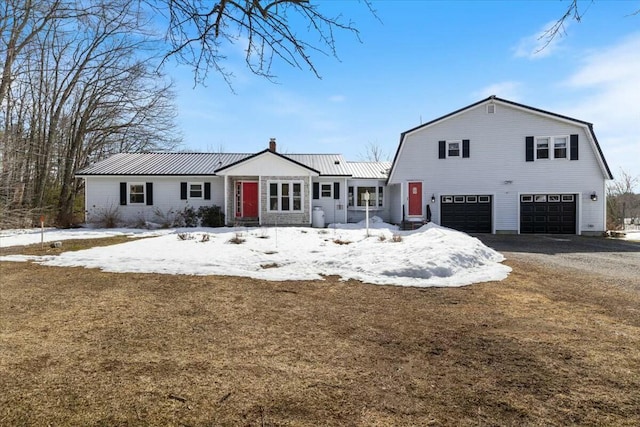 view of front of home featuring driveway, a gambrel roof, a chimney, a garage, and metal roof