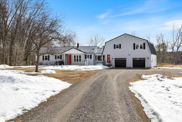 colonial inspired home featuring an attached garage, a gambrel roof, a chimney, metal roof, and driveway