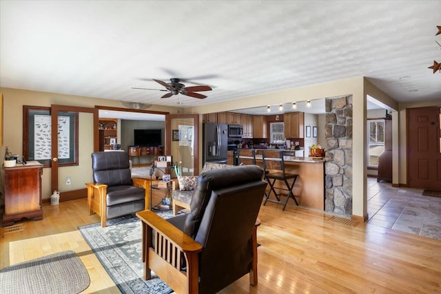 living area featuring light wood-style flooring, visible vents, baseboards, and ceiling fan