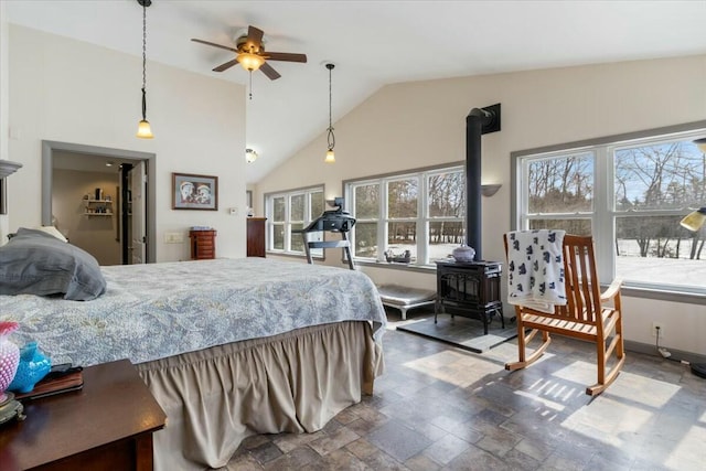 bedroom with a wood stove, baseboards, high vaulted ceiling, and stone finish floor